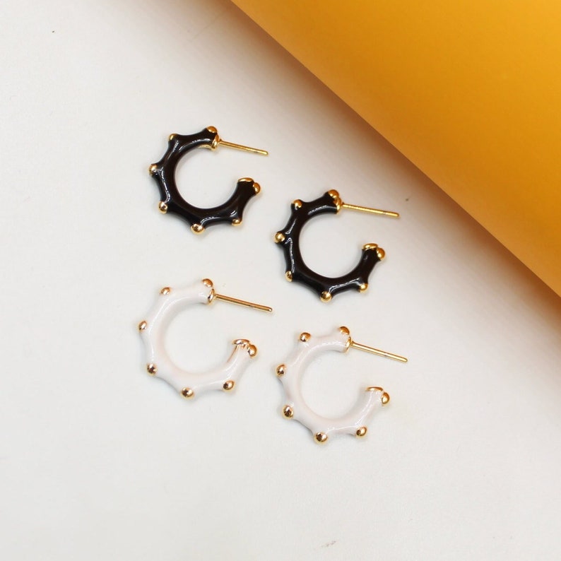 Two pairs of chic black and white enamel hoop earrings featuring gold bead accents rest on a neutral surface.