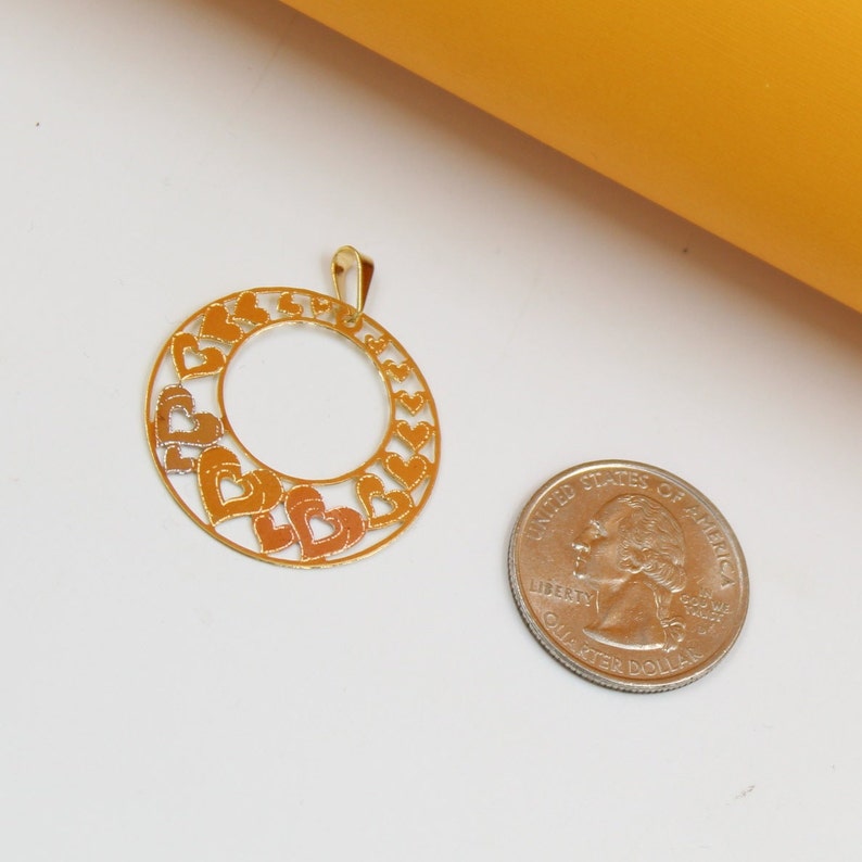 A gold heart pendant rests next to a US quarter coin on a white surface to show scale.