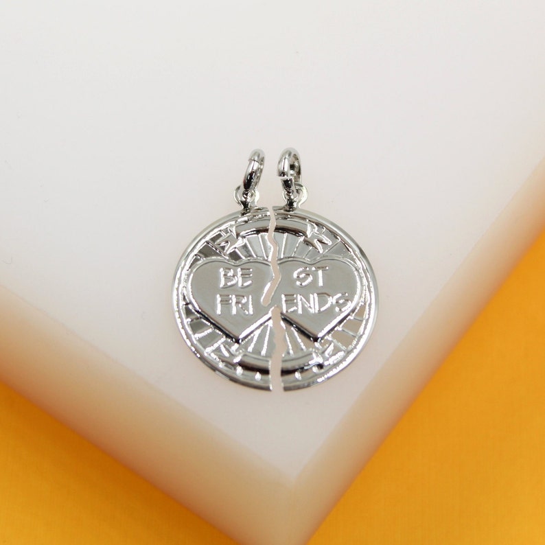 A silver best friends split circle pendant rests on a white surface against an orange backdrop.
