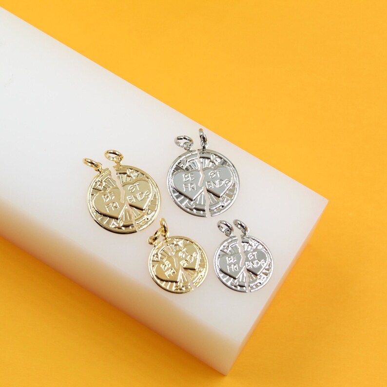 Two pairs of gold and silver "Best Friends" split-heart round charms rest on a white block against a yellow background.