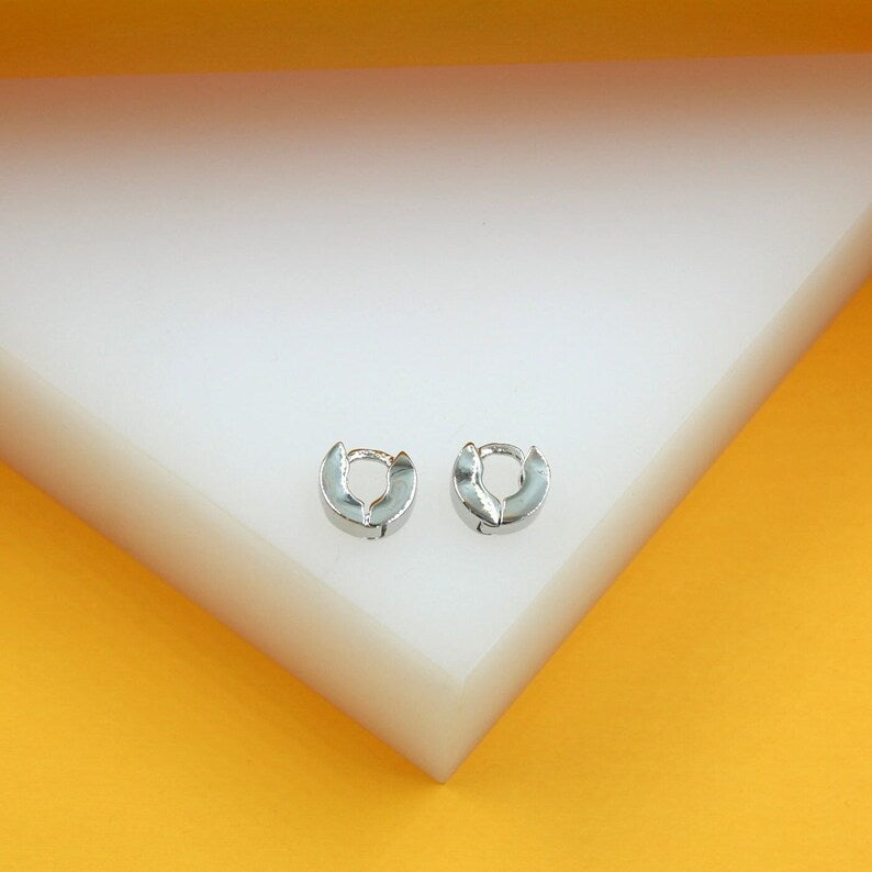A pair of sleek silver hoop earrings rests neatly on a white and yellow display stand.
