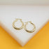 A pair of polished gold hoop earrings rests on a white display surface against a vibrant yellow background.