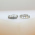 Two silver huggie hoop earrings sit on a neutral surface, showcasing a sparkling pavé crystal front on one and delicate cut-out hearts along the side of the other.