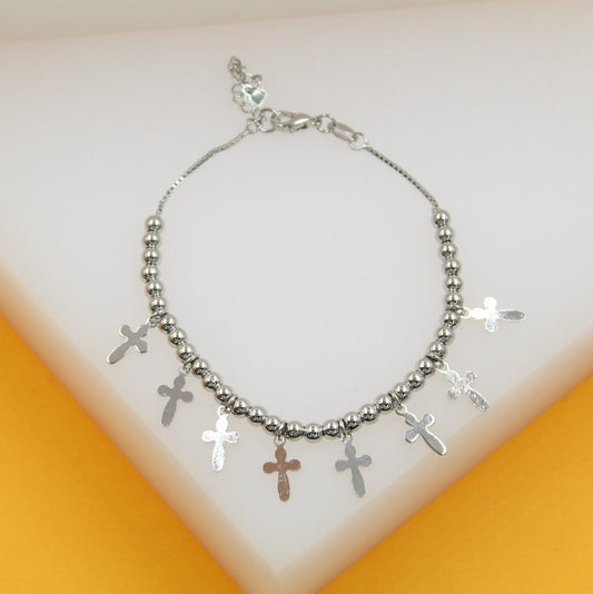 A silver bead charm bracelet features multiple hanging cross pendants against a neutral white and yellow background.