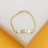 A gold identification bracelet with a curb chain rests on a white display surface.