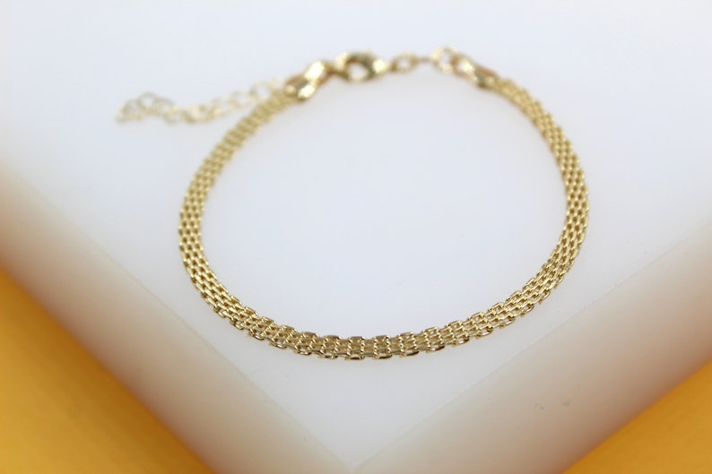 A delicate gold mesh chain bracelet rests on a smooth white surface.