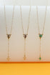 Three gold pearl rosary necklaces with colorful religious pendants and matching crosses hang vertically on a light background.