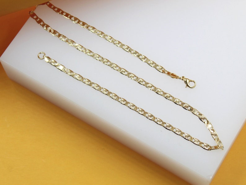 A gold-plated chain lies on a white display surface, showcasing its shiny, interlocking links and classic design.