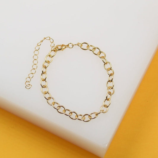 A delicate gold chain-link bracelet lies on a white surface against a warm yellow backdrop.