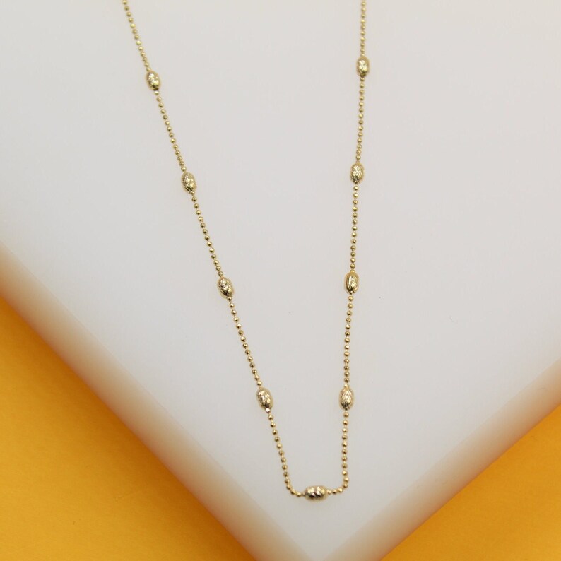 A delicate gold bead chain necklace rests gracefully on a white display surface.
