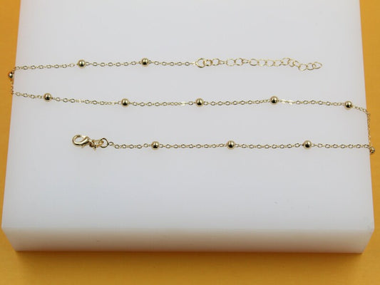 A delicate gold chain bracelet features evenly spaced small golden beads and an adjustable clasp, resting flat on a white display surface.