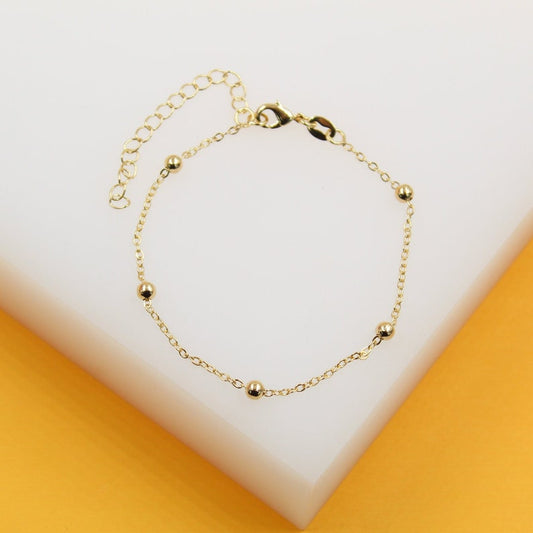 A delicate gold chain bracelet features evenly spaced shiny bead accents on a white display surface.