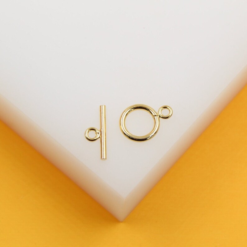 A shiny gold toggle clasp rests on a white display against an orange background.