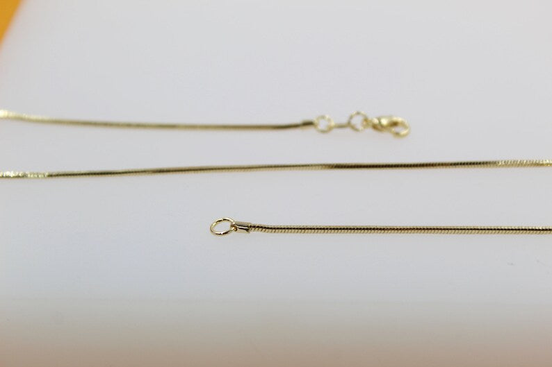 A thin gold snake chain necklace displays its clasp and delicate links against a clean white background.