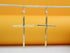 A pair of elegant gold cross dangle earrings hangs suspended against a bright yellow background.