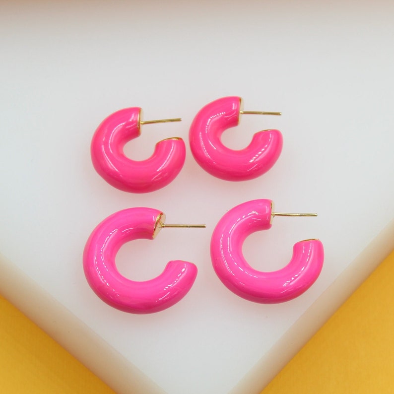 Two pairs of vibrant neon pink enamel hoop earrings rest on a clean white display surface.