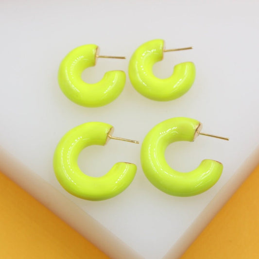 Four vibrant neon green enamel hoop earrings rest on a white surface against a yellow background.