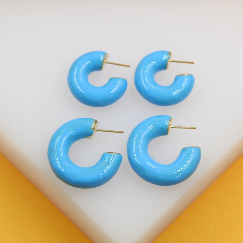 Four vibrant turquoise enamel hoop earrings with gold posts rest neatly on a white display surface.