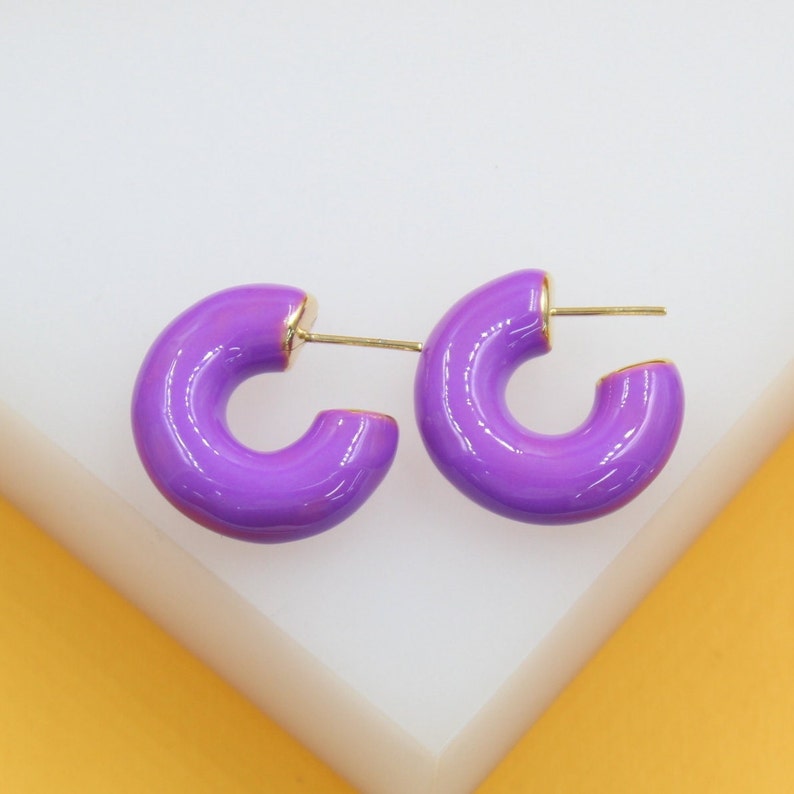 Glossy purple enamel hoop earrings rest on a white display stand against a bright yellow background.