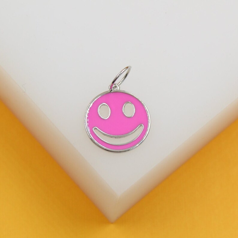 A silver-rimmed pink smiley face charm rests on a white and yellow display block.