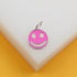 A silver-rimmed pink smiley face charm rests on a white and yellow display block.