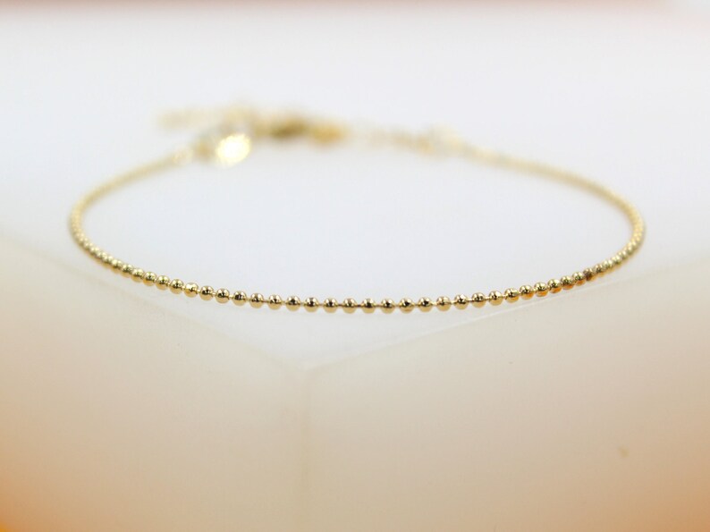 A delicate gold beaded bracelet rests on a white display surface.