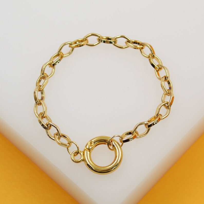 A delicate gold chain bracelet features a secure spring ring clasp, resting neatly on a neutral white display surface.