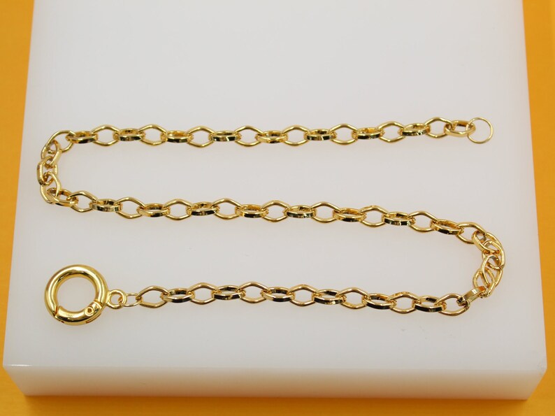 A shiny gold-plated jewelry chain with interlocking oval links lies flat on a white display block.