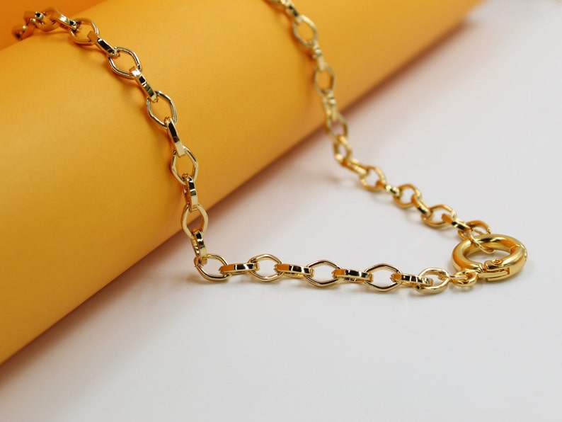 A shiny gold chain necklace rests against a warm yellow and white background.
