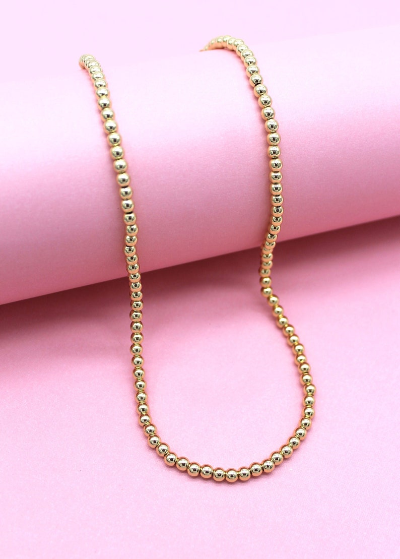 A glossy gold beaded necklace rests gracefully against a soft pink background.