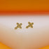 A pair of gold cross stud earrings adorned with sparkling cubic zirconia stones rests upright on a light display surface.