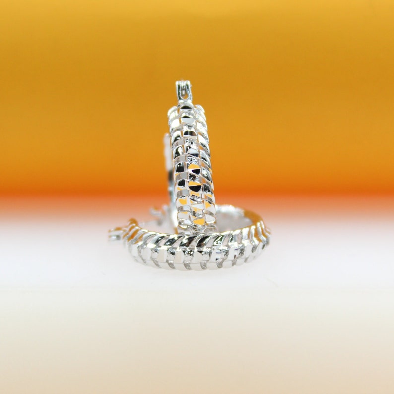 A pair of textured silver hoop earrings sits against a warm, gradient yellow and white background.