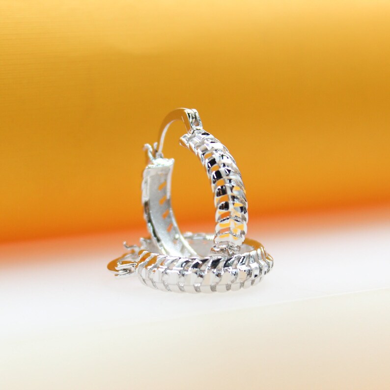 A pair of textured silver hoop earrings rests against a warm orange and white background.