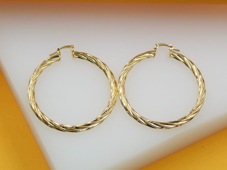 A pair of polished gold twist hoop earrings rest on a white surface.