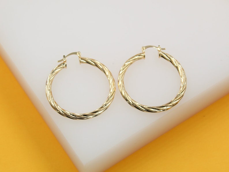 A pair of elegant twisted gold hoop earrings rests neatly on a smooth white display surface.