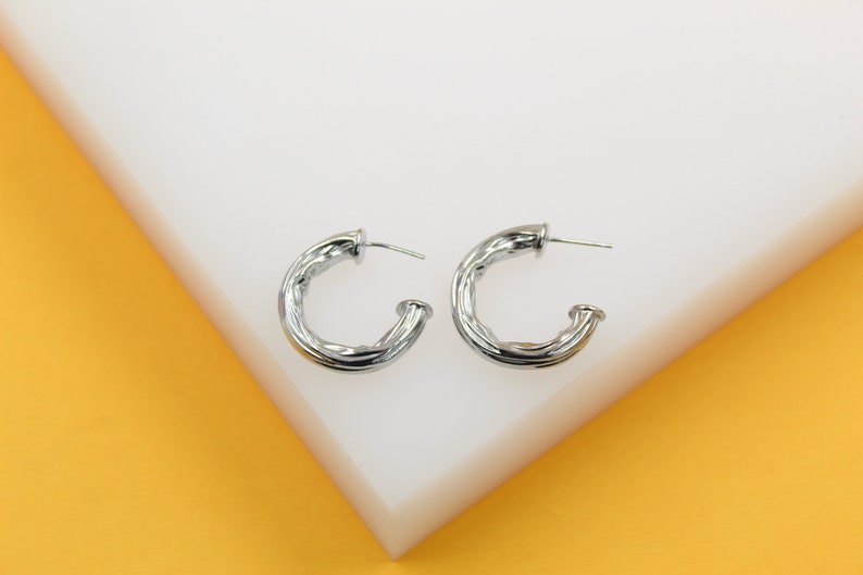 A pair of silver twisted chunky hoop earrings rests on a white display surface.