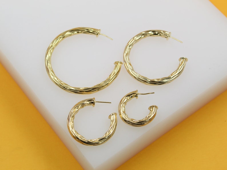 A set of four gold twisted hoop earrings in descending sizes rests on a white display surface.