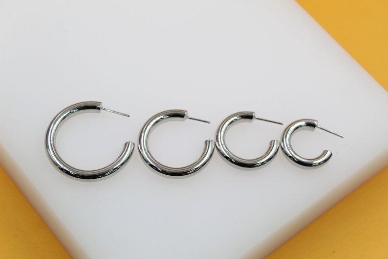 Four polished silver hoop earrings display a graduated size range from largest to smallest on a white display surface.
