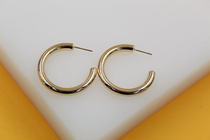 A pair of thick gold hoop earrings rests side by side on a clean white display surface.