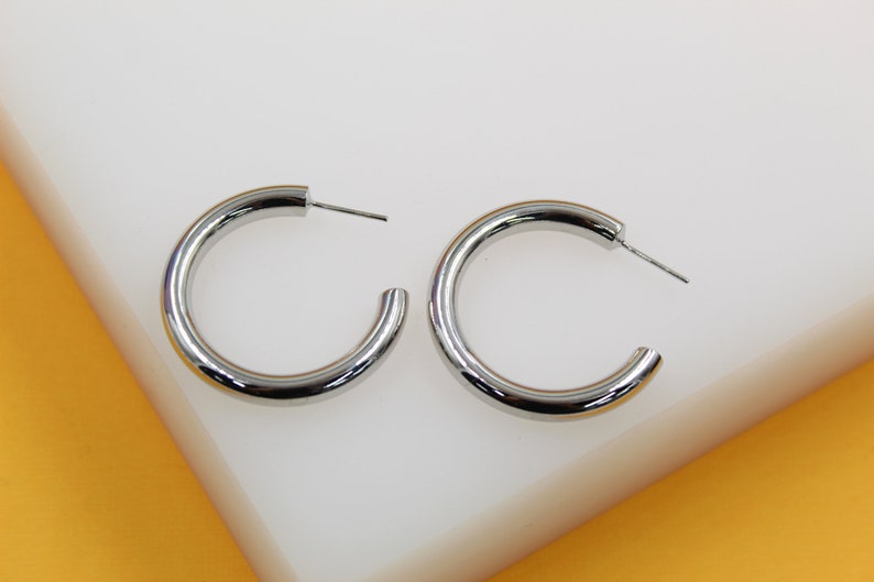 A pair of polished silver hoop earrings rest on a white surface.