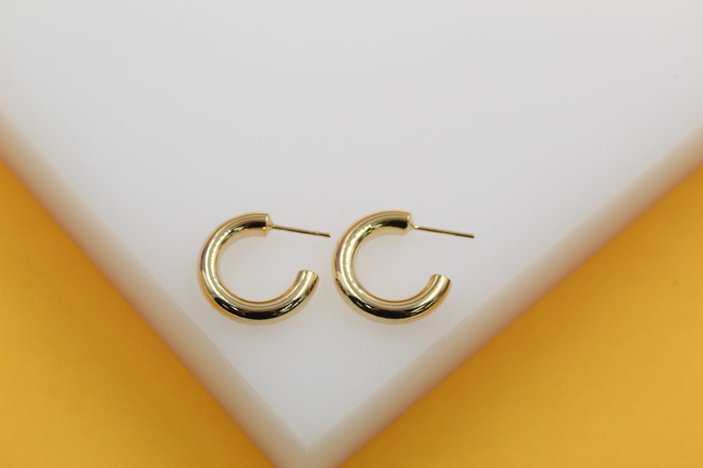 A pair of polished gold hoop earrings rests neatly on a white display surface.