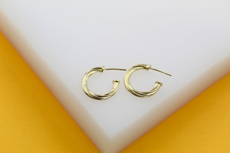 A pair of shiny gold-plated twisted hoop earrings rests on a white display surface.