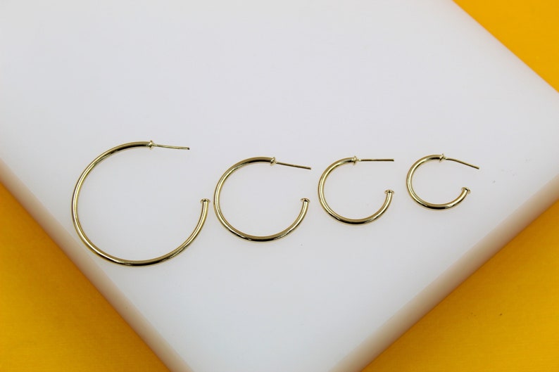 Four graduated gold hoop earrings are displayed in a row on a white and yellow display stand.