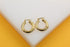 A pair of thick gold hoop earrings rests on a white display surface against a vibrant yellow background.