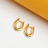 A pair of sleek, gold-plated U-shaped huggie earrings rests on a clean white and yellow surface.