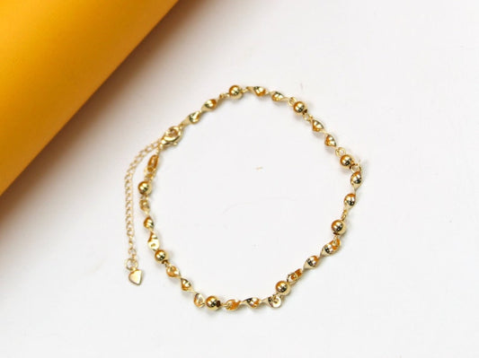 A delicate gold-plated bracelet featuring alternating polished beads and twisted links rests on a clean white surface.