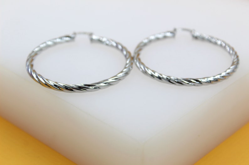 A pair of polished silver twisted hoop earrings rests on a white display surface.