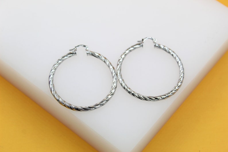 A pair of polished silver twist hoop earrings rests on a white display surface.