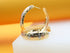A pair of elegant tri-color gold hoop earrings rests on a white display surface against a warm yellow background.
