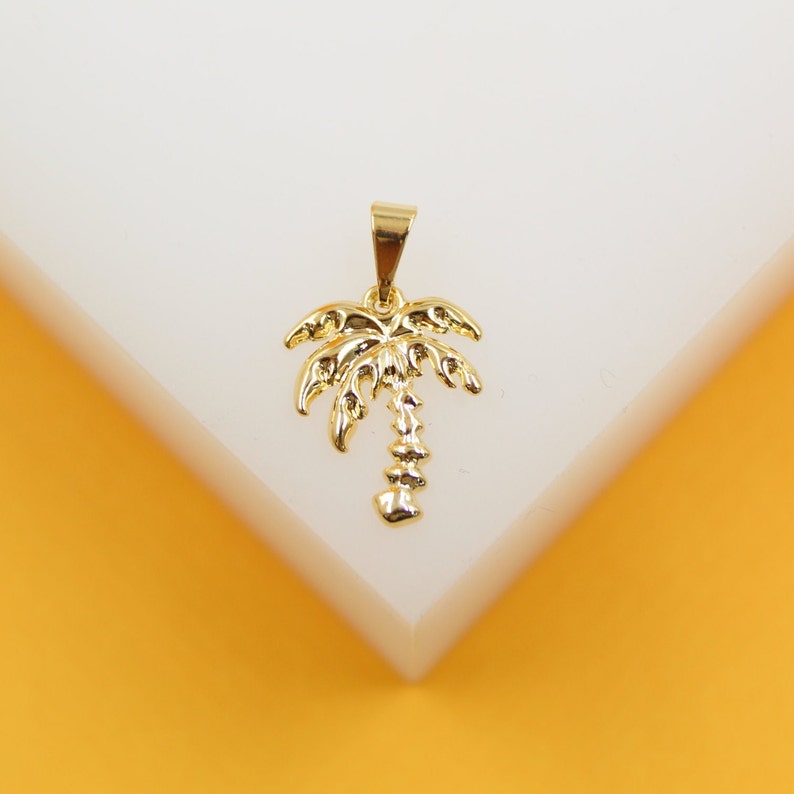 A gold palm tree pendant rests on a white display against a warm yellow background.